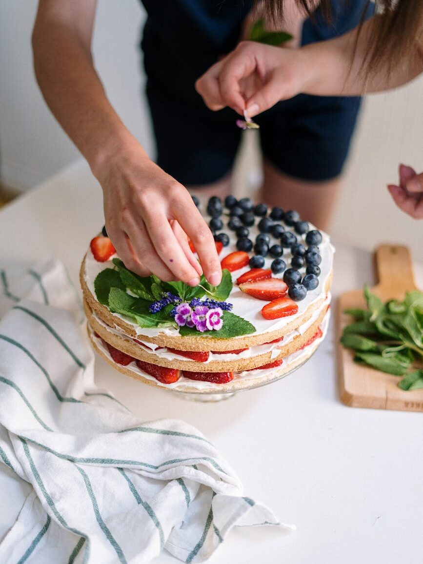 person decorating cake with different berries